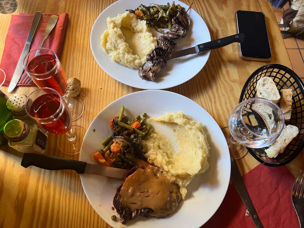 Deux assiettes remplies de nourriture posées sur une table en bois, autour des verres remplis de vin