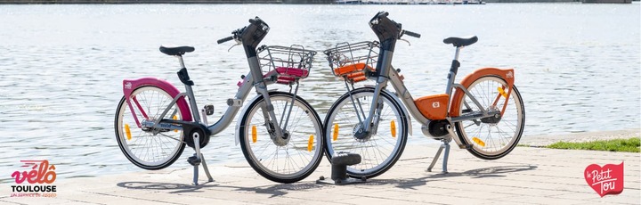deux vélos éléctriques et classiques rose et orange devant la garonne à toulouse